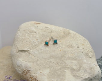 Puede incluir: Dos anillos de nariz con piedras turquesa engastadas en un marco cuadrado. Los anillos de nariz son de oro y plata.
