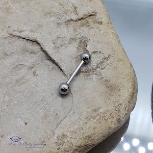 May include: A silver barbell with two round balls on each end. The barbell is lying on a light brown rock.
