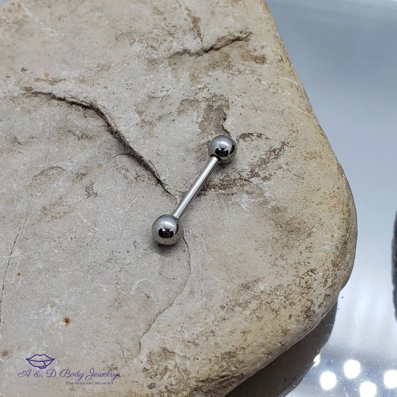 May include: A silver barbell with two round balls on each end. The barbell is lying on a light brown rock.