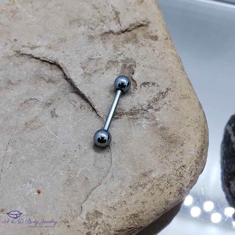 May include: A silver barbell with two round balls on each end. The barbell is on a gray rock.