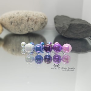 May include: A set of six iridescent belly button rings with different colored beads. The beads are in shades of blue, purple, and pink. The rings are made of surgical steel.