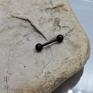 May include: Black barbell with black balls on each end. The barbell is on a light brown rock surface.