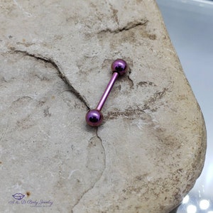 May include: A purple titanium barbell with rounded ends. The barbell is on a gray rock surface.
