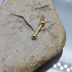 May include: Gold barbell with two round balls on each end. The barbell is lying on a light brown rock.