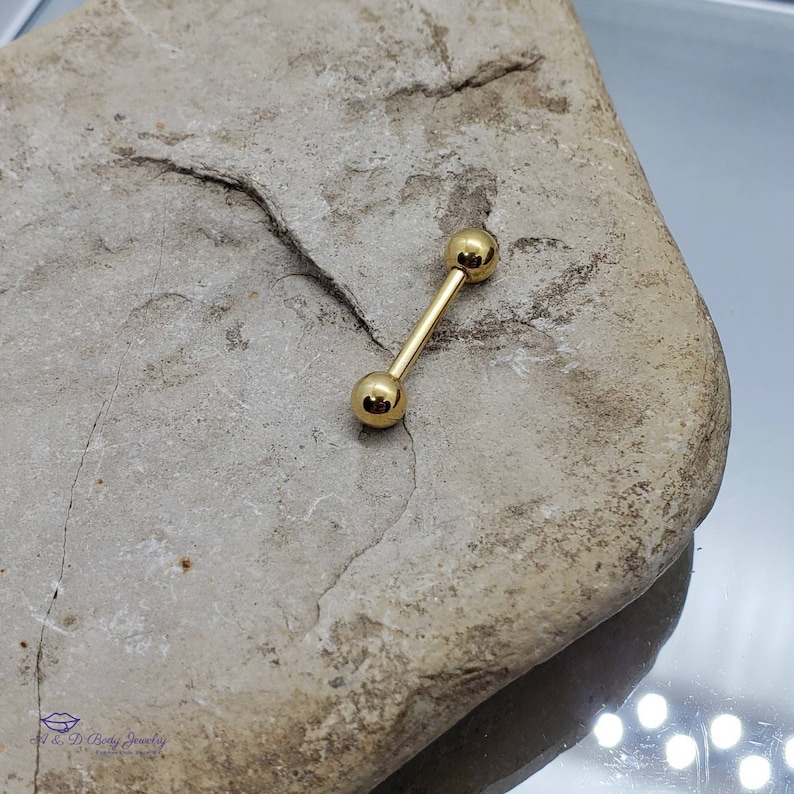 May include: Gold barbell with two round balls on each end. The barbell is lying on a light brown rock.