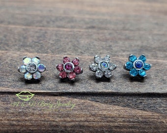 May include: Four flower-shaped body jewelry pieces with different colored gems. The pieces are made of surgical steel and have a silver finish. The gems are clear, pink, white, and blue.