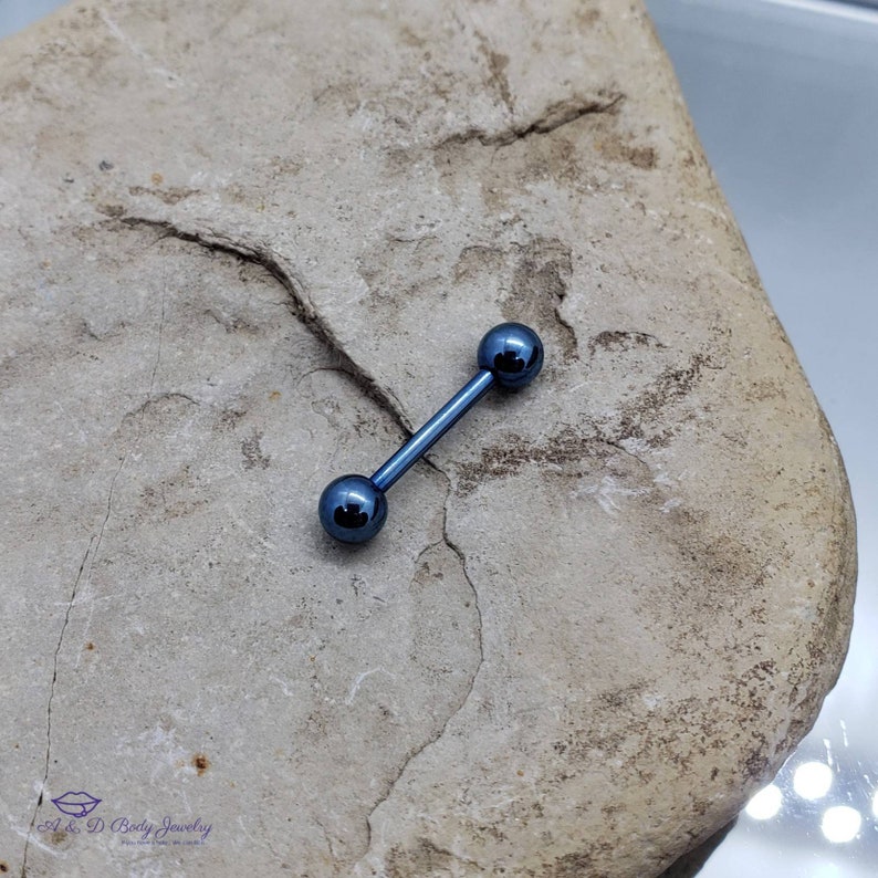 May include: A blue titanium barbell with two round balls on each end. The barbell is lying on a gray rock.