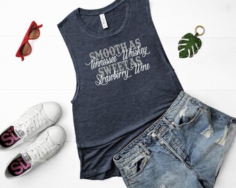 May include: A navy blue sleeveless tank top with the text "Smooth as Tennessee Whiskey Sweet as Strawberry Wine" printed in silver on the front. The tank top is paired with denim shorts and white sneakers.