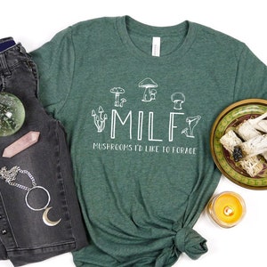 May include: A green t-shirt with a white graphic of mushrooms and the text "MILF Mushrooms I'd Like to Forage".