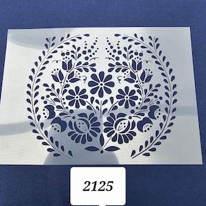 May include: A white stencil with a black floral design in a circle. The design features a wreath of leaves and flowers. The number 2125 is written in the bottom right corner of the image.