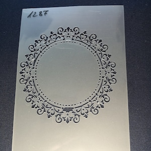 May include: A white plastic stencil with a black ornate circular design. The stencil is labelled "1287".