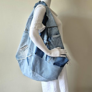 May include: A large hobo-style shoulder bag constructed from repurposed light and medium-wash denim fabric. The bag features a patchwork design with visible seams, frayed edges, and integrated pockets from original jeans, including a metal zip.