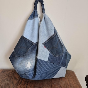 Op de afbeelding: Een grote patchwork denim tote bag met een gefronsde handgreep. De tas is gemaakt van verschillende tinten blauwe denim, waaronder licht gewassen, donker gewassen en gestreepte stoffen. Voorzien van twee denim zakken en een rood label.