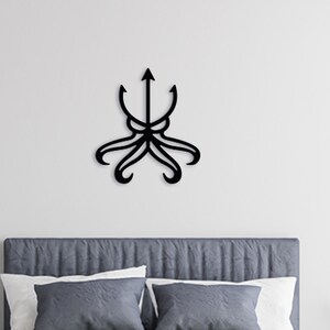 May include: Black metal wall decor in the shape of an octopus with a trident on top. The decor is mounted on a white wall above a gray headboard with two pillows.