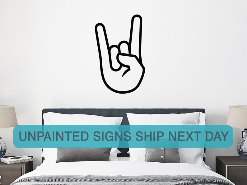 May include: Black and white wall decal of a hand making the rock and roll hand gesture. The decal is on a white wall above a bed with gray bedding and white pillows. The text "UNPAINTED SIGNS SHIP NEXT DAY" is in a blue box at the bottom of the image.