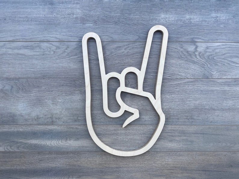 May include: A white wooden cutout of a hand making the rock and roll hand gesture. The hand is outlined in white against a wood grain background.