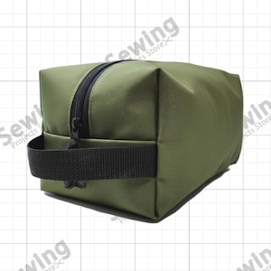 May include: Olive green rectangular travel bag with a black zipper and a black handle. The bag is made of a durable, textured fabric. The bag is designed to hold toiletries and other travel essentials.