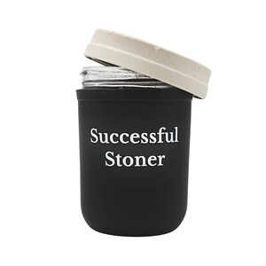 Könnte beinhalten: Schwarzer Silikonbehälter mit weißem Deckel und dem Aufdruck "Successful Stoner" auf der Seite.