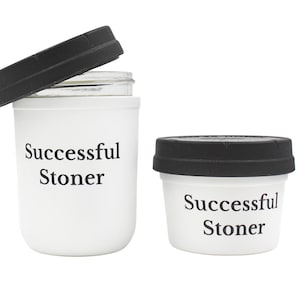 Könnte beinhalten: Zwei weiße Behälter mit schwarzen Deckeln. Der größere Behälter hat ein Glasgefäß im Inneren. Beide Behälter tragen den Aufdruck "Successful Stoner".