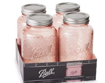May include: A set of four 32 oz Ball mason jars in a rose-tinted glass with a textured finish and silver-colored metal lids. The jars are housed in a black cardboard display box labeled Collectors Edition 1923-1933 with the Ball brand logo.