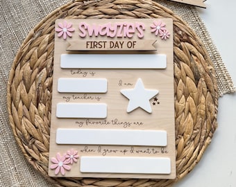 May include: A wooden sign for the first day of school, with the text "Swayzie's FIRST DAY OF" in pink. The sign has spaces to write "today is", "I am", "my teacher is", "my favorite things are", and "when I grow up I want to be". A separate sign says "LAST DAY OF".