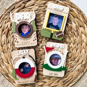 May include: Four wooden Father's Day photo frames with decorative elements. One frame has deer antlers and the text "DAD". Another has a football theme. The third has a fishing theme, and the fourth has a golf theme. Each frame has a photo of a child.