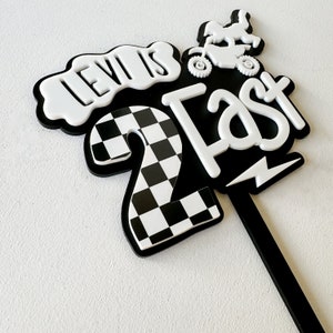 Black and white layered acrylic 'Two Fast' second birthday cake topper showing bold number and text design, on a black acrylic stake