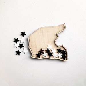 May include: Wooden cutout of a race track with black and white star-shaped pieces scattered inside.