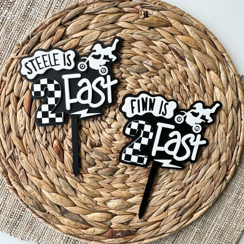 Two layered acrylic 'Two Fast' second birthday cake toppers in black and white checkered design, styled as a set with dirt bike motif