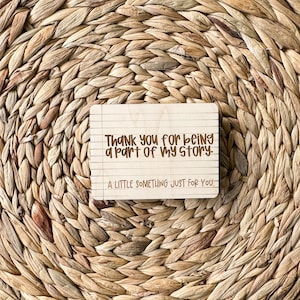 May include: A wooden sign with the text "Thank you for being a part of my story. A little something just for you." The sign has a lined paper background.