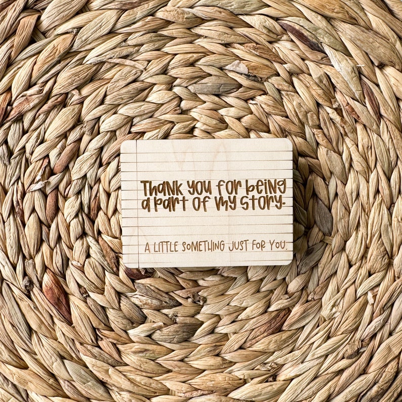 May include: A wooden sign with the text "Thank you for being a part of my story. A little something just for you." The sign has a lined paper background.