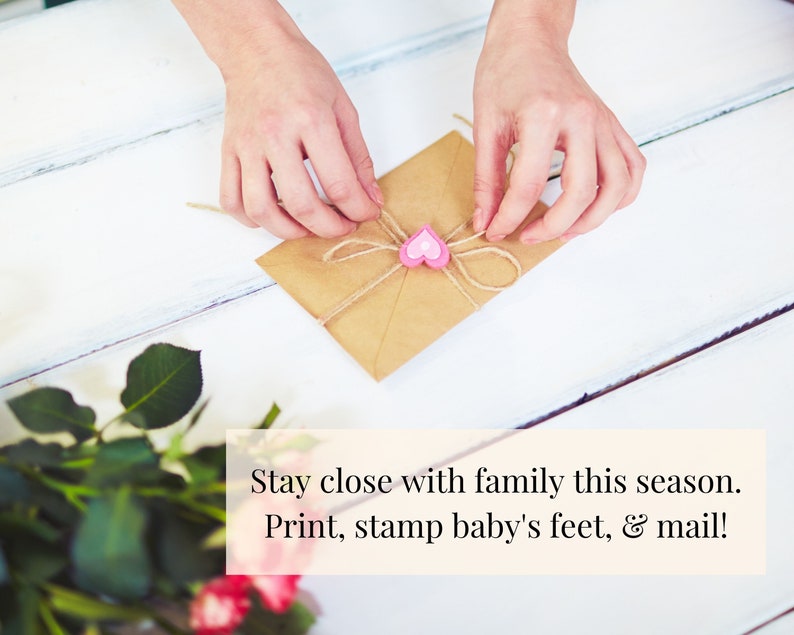 May include: A brown envelope tied with twine and a pink heart charm. The text "Stay close with family this season. Print, stamp baby's feet, & mail!" is written below the envelope.