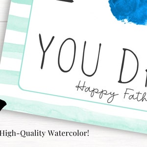 May include: A light blue and white striped card with the text "You Da" and "Happy Father's" in black cursive writing.