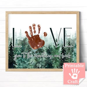 May include: Printable art print with a watercolor forest background and the word "LOVE" in black text. A brown handprint is in the center of the print. The text "you to the mountains and back" is below the word "LOVE".