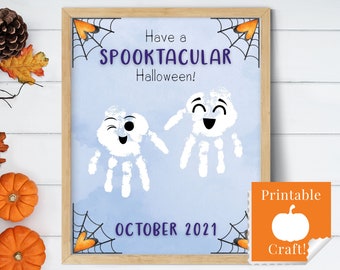 May include: Printable Halloween craft with the text "Have a Spooktacular Halloween!" and "October 2021". The craft features two white handprint ghosts with faces on a blue background with black spiderwebs in the corners. The bottom right corner has a separate orange square with the text "Printable Craft!" and a white pumpkin silhouette.