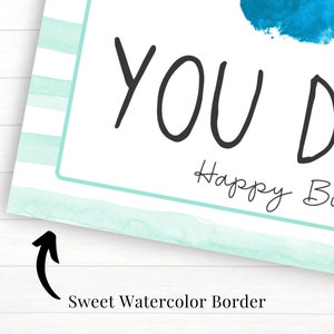 May include: A light blue watercolor border with white stripes surrounds a white card with the text "You Da" and "Happy Birth".