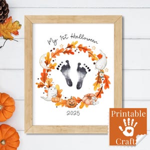 Puede incluir: Una impresión enmarcada con temática de Halloween. La obra de arte presenta huellas de bebé rodeadas por una corona de hojas, calabazas, fantasmas y el texto "My 1st Halloween 2025". Un sello en la esquina inferior derecha dice "Printable Craft".