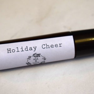May include: A black roller bottle with a white label that says "Holiday Cheer" and a small logo that says "oil & herb".