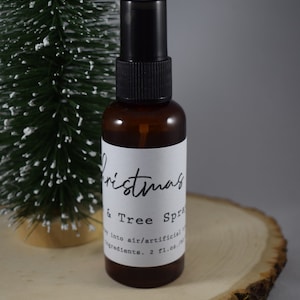 Könnte beinhalten: Eine braune Glasflasche mit einer schwarzen Sprühdüse und einem weißen Etikett mit der Aufschrift "Christmas & Tree Spray" mit dem Text "Spray into air/artificial ingredients. 2 fl.oz."
