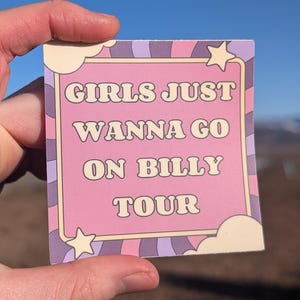 May include: A square sticker with the text "GIRLS JUST WANNA GO ON BILLY TOUR" in a retro font. The sticker has a pink background with a light purple and white border and star accents.