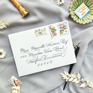 May include: A white envelope with elegant calligraphy, addressed to Mrs. Marielle Hudson-Roy, with stamps featuring botanical and wildlife illustrations. A gold wax seal and pen are also visible, suggesting a vintage or artistic theme.