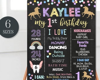 May include: A printable chalkboard style sign for a first birthday party. The sign is decorated with rainbows, stars, and unicorns. It features the name Kaylee and details about the child's first year, including weight, height, and favorite things. The sign is customizable and can be edited with a computer.