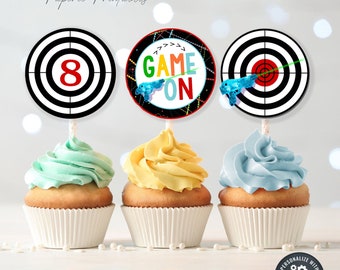 May include: Three cupcake toppers featuring a black and white target with a red center, a black and white target with a red center and a green laser beam, and a black and white target with a red center and the text "GAME ON" in rainbow colors. The cupcake toppers are printed on white cardstock.