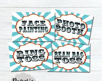 May include: Four printable signs with a circus theme. The signs are blue and white with red and yellow accents. The signs say "Face Painting", "Photo Booth", "Ring Toss", and "Bean Bag Toss".