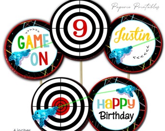 May include: Four 6-inch round printable laser tag party cupcake toppers. The toppers feature a black and white target design with a red bullseye, a green laser beam, and a blue toy gun. The text on the toppers reads "Game On", "9", "Justin", and "Happy Birthday".