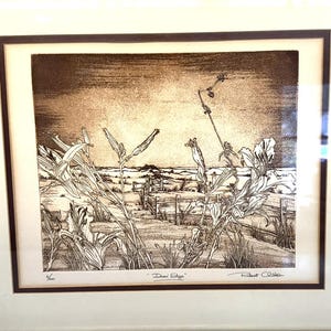 May include: Framed sepia-toned print of a landscape with tall grasses and a distant shoreline. The artwork, titled "Dune Edge" by Robert O'Brien, is in a gold-colored frame with a cream-colored mat.