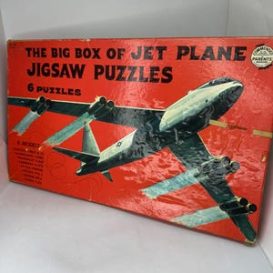 May include: A red box with a picture of a jet plane on it. The box says "The Big Box of Jet Plane Jigsaw Puzzles" and "6 Puzzles". The box also lists 8 models of jet planes.