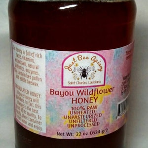 May include: A glass jar of Bayou Wildflower Honey with a red lid. The label reads "Just Bee Apiary" and "100% Raw, Unheated, Unpasteurized, Unfiltered, Unprocessed." Net weight is 22 oz (624 g).