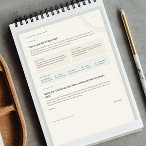 Op de afbeelding: Een spiraalgebonden notitieboekpagina met de titel How to use this 30-day reset, voorzien van gedrukte tekst, instructiesecties en een genummerde reeks. Een potlood met marmerpatroon rust aan de rechterkant van het witte papier, waarop secties staan zoals Notice first. Decide second. Move before you feel completely ready.