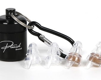 May include: Black cylindrical case with the text "Placid Sound" in white script, attached to a black carabiner clip. Clear earplugs are next to the case. The earplugs have a brown filter.